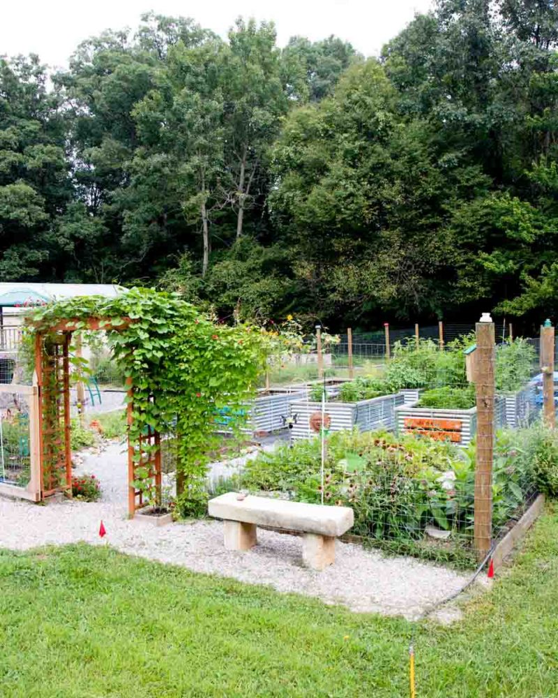 A concrete bench sits outside a fenced in raised bed garden.