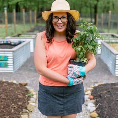 Brunette woman standing in a garden and holding a tomato plant, smiling