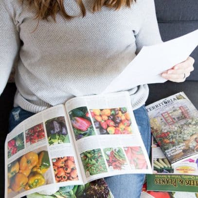 A brunette woman consults a piece of paper while looking at seed catalogs.