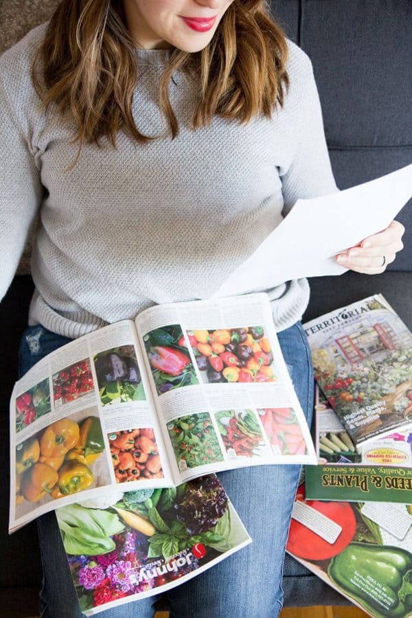 A brunette woman consults a piece of paper while looking at seed catalogs.