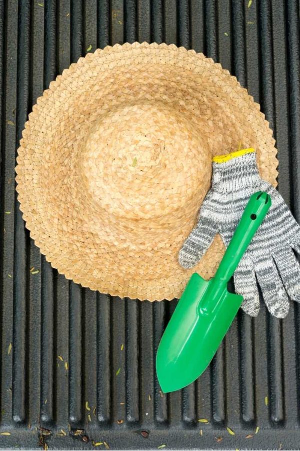A green trowel and a striped garden glove sits on top of a straw gardening hat