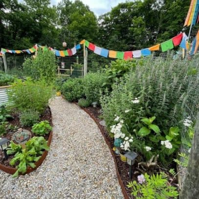A pollinator garden with prayer flags and a weed-free gravel aisle