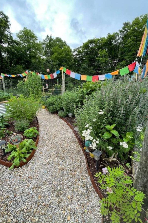 A pollinator garden with prayer flags and a weed-free gravel aisle