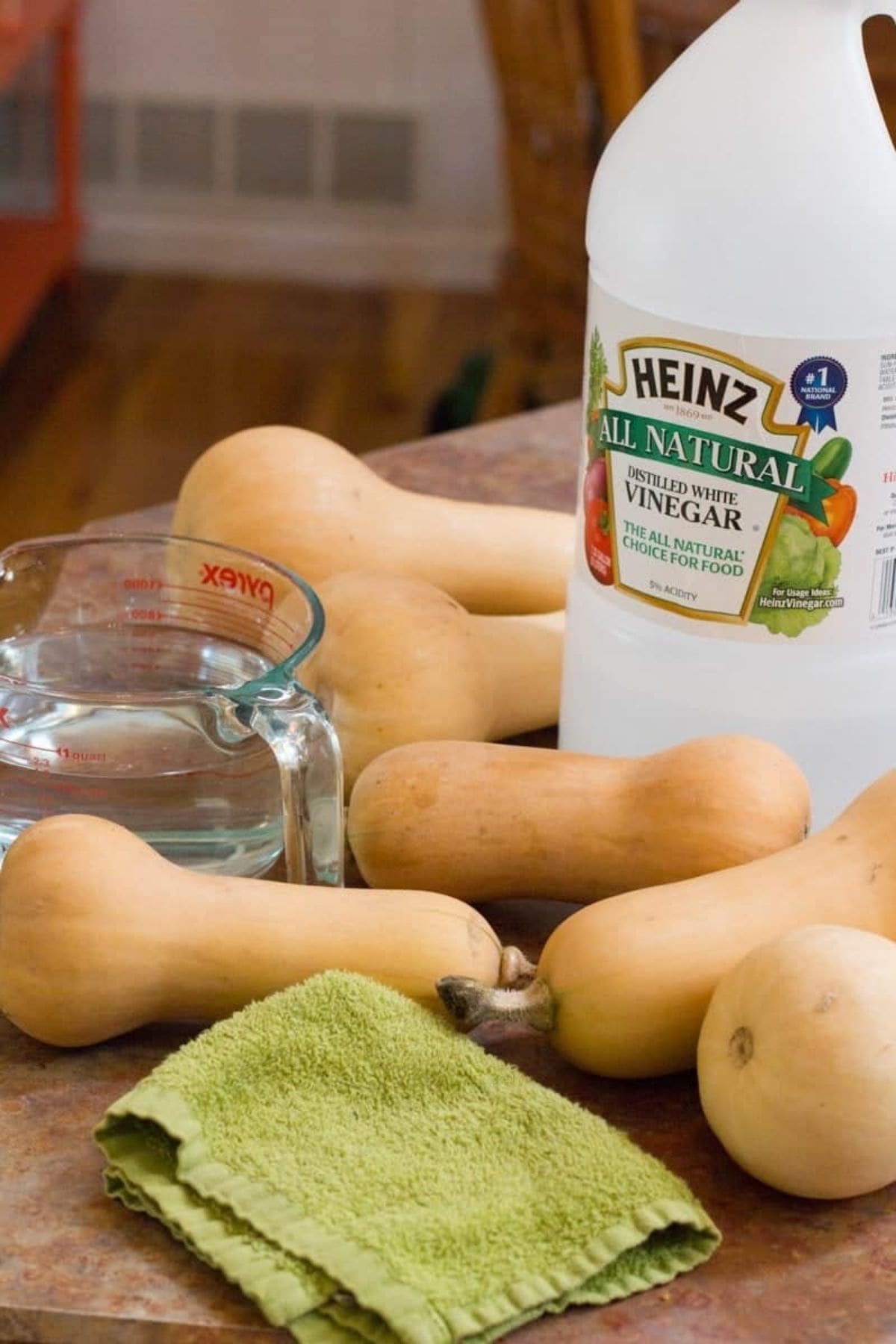 Butternut squash lay on a table in front of a jug of white vinegar.